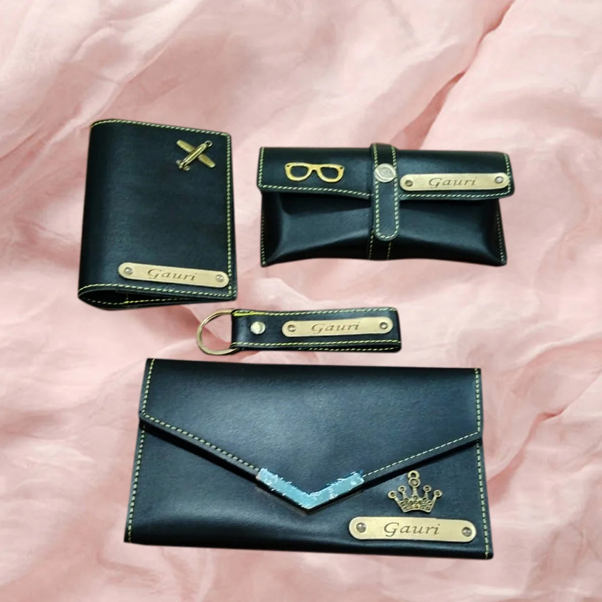 Set of black leather accessories with gold accents on a pink fabric background