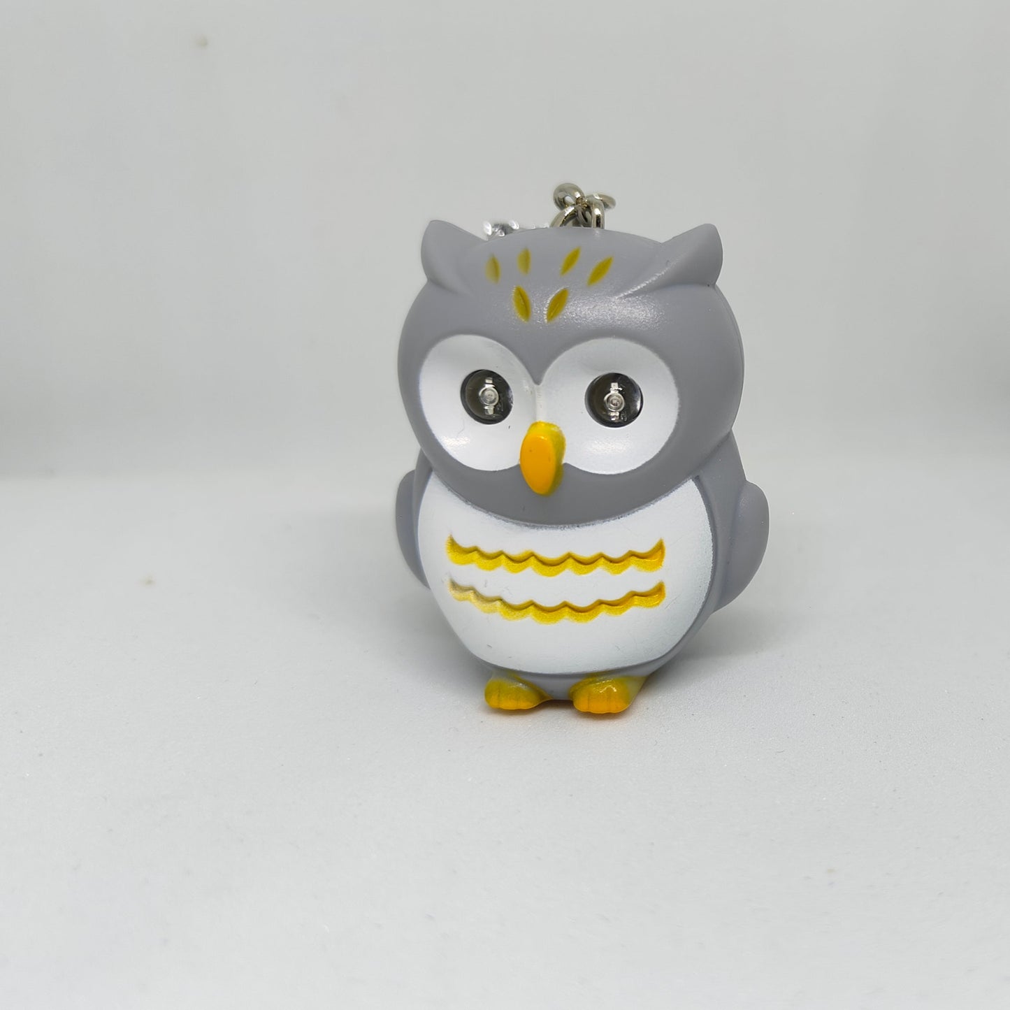 Gray owl-shaped keychain with yellow accents on a white background